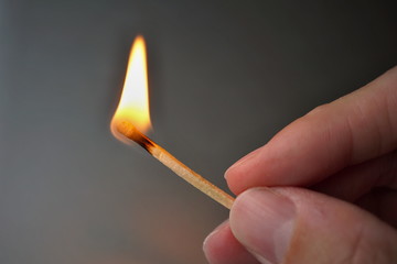 Male hand holding burning safety match stick with a flame getting close to the hand