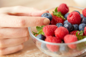 close up of young woman hand with berries in bowl