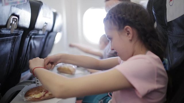 Young woman sits in chair near illuminator of airplane and eats meal for passenger