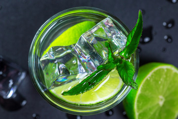 Mojito cocktail with lime, ice cubes and mint in highball glass on a black background Copy space