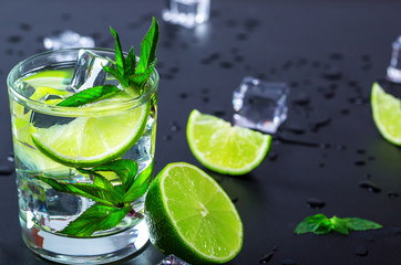 Mojito cocktail with lime, ice cubes and mint in highball glass on a black background Copy space