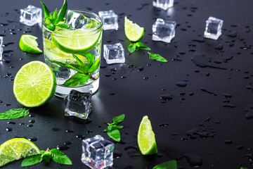 Mojito cocktail with lime, ice cubes and mint in highball glass on a black background Copy space