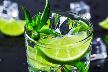 Mojito cocktail with lime, ice cubes and mint in highball glass on a black background Copy space
