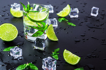 Mojito cocktail with lime, ice cubes and mint in highball glass on a black background Copy space
