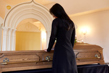 sad woman with coffin at funeral in church