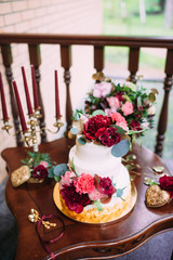 Wedding cake decorated with red, pink peony flowers, standing on golden plate with two golden spoon