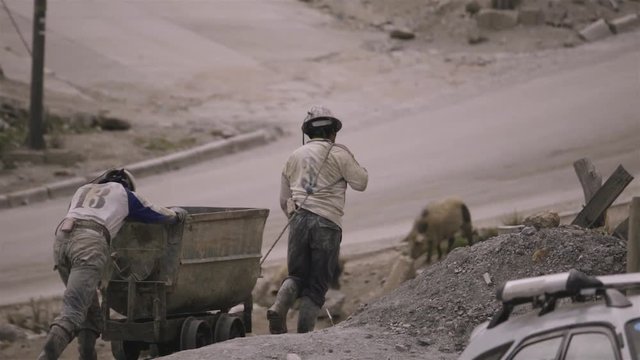 Couple of miners pulling a cart full of mineral passing through the tunnel. Bolivia