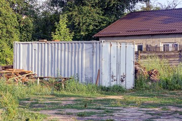 Fototapeta na wymiar Серый железный контейнер стоит в траве возле дома