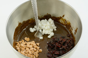Brownie or chocolate cake batter with caramel chips, dried cranberries and marshmallow bits in stainless steel mixing bowl 