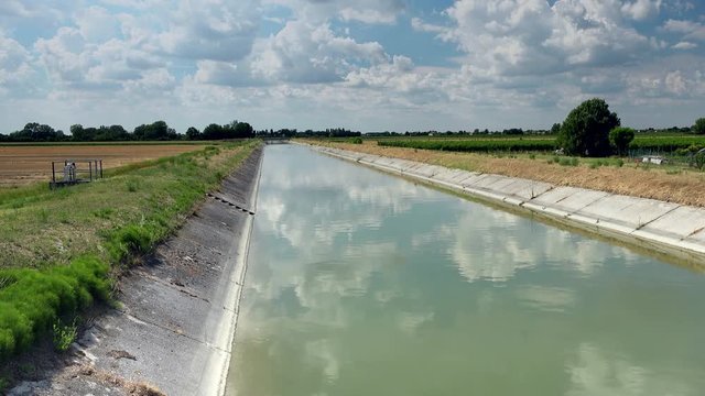 Engineering built this artificial canal to bring water to cultivated fields, here flowing peaceful under a summer blue sky of white clouds, ungraded shot