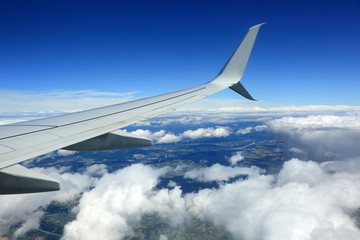Widok skrzydła samolotu, chmur, i obszarów zabudowanych z lotu ptaka. - obrazy, fototapety, plakaty
