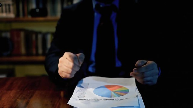 A nervous boss drops disappointing papers with charts, then gestures at us with his fingers like he chose us to fix it.
