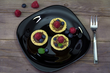 A delicious dessert with vanilla and chocolate pudding  in a basket on the black plate with fresh raspberries and blueberries. Light summer sweets