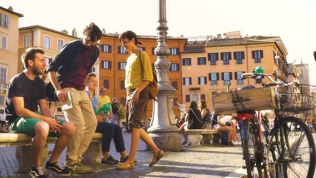 Friends sitting on a bench in crowded Square in Rome