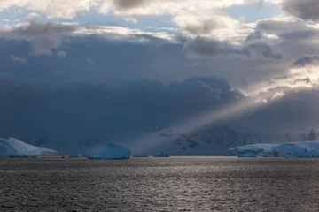 Fotobehang Stom clouds with light beam hitting icebergs along the Antarctic Peninsula. © David