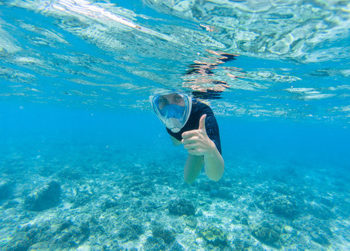 Woman snorkeling in turquoise sea water. Snorkel shows thumb in full face mask.
