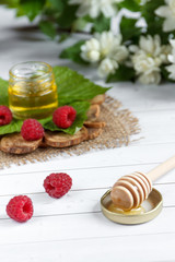 The bowl with honey, berries and leaves of raspberry on a wooden stand. Spoon with honey, Jasmine flowers