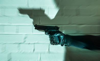 ein Täter hält eine Waffe in der Hand, an einer Mauer ist der Schatten zu sehen