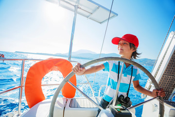 Little boy captain on board of sailing yacht on summer cruise. Travel adventure, yachting with...