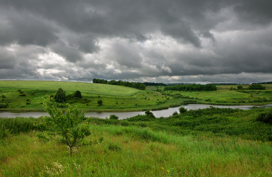 Cloudy summer scene with small river. Dramatic sky over the fields