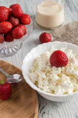 cheese in white plate with strawberries on a wooden table with canvas tablecloth.