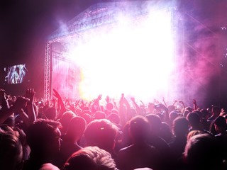 A crowd with their hands up in the air under the scene in red  and purple smoke