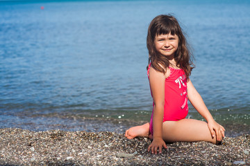 a young girl in a red swimsuit posing on the shore of the sea