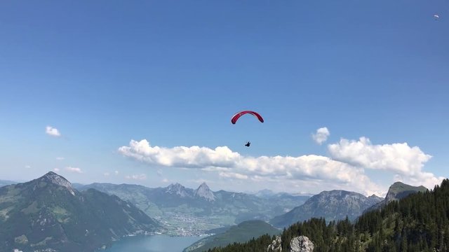 Paragleiter / Gleitschirm fliegt und kreist &uuml;ber den Schweizer Alpen und dem Vierwaldst&auml;ttersee im blauen Himmel. Im Hintergrund Schweizer Berge Mythen, Wildspitz, Uri Rotstock