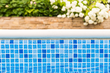 Mosaic blue swimming pool border with flowers and green garden on the background