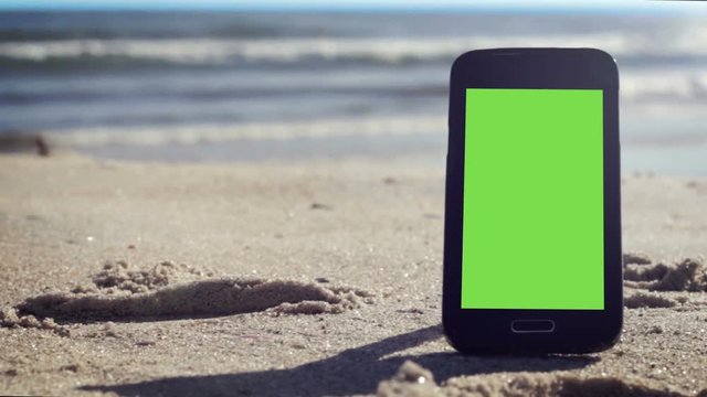 Generic black smart phone with green screen on the beach in Brazil, ready to key and replace.