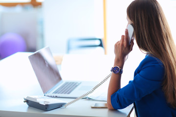 Portrait of a young woman on phone in front of a laptop computer