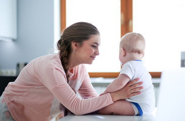 Mother with her baby in the bright kitchen at home.