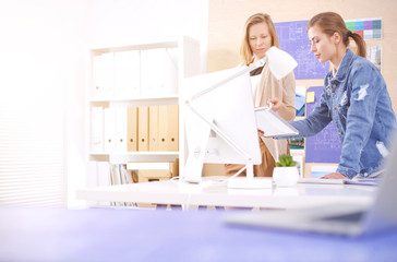 Two young woman standing near desk with instruments, plan and laptop.