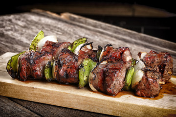 Cooked beef kebabs with vegetables and spices on wooden board 