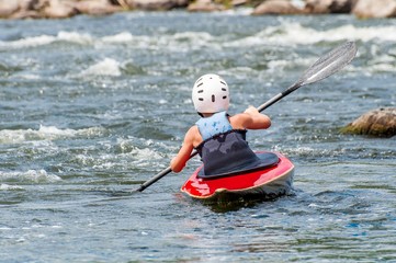 A teenager trains in the art of kayaking. Slalom boats on rough river rapids. The child is...