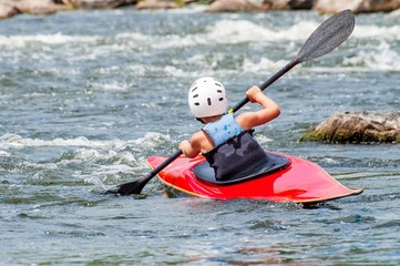 A teenager trains in the art of kayaking. Slalom boats on rough river rapids. The child is...