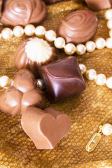 Chocolates and pearls on golden background