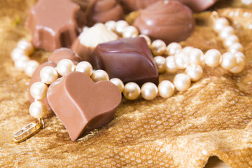 Chocolates and pearls on golden background