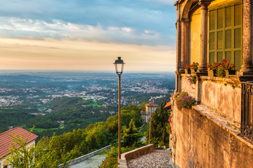 Sacro Monte of Varese (Santa Maria del Monte), medieval village, Italy. Picturesque view of the final part of the sacred road with the 14th chapel, Varese, on the horizon the city of Milan, at dawn - obrazy, fototapety, plakaty