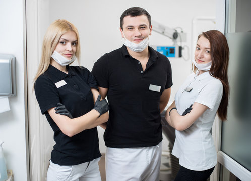 Portrait of male dentist and two female assistants in dental office. Women are standing with hands crossed and looking to the camera