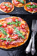 Homemade pizza with prosciutto, tomato, arugula on black slate board. Close up.