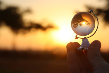 male hand holding small crystal globe in front of sunset