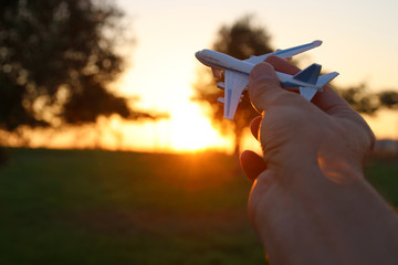 close up of man's hand holding toy airplane against sunset sky