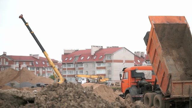 Construction vehicles and builders on construction site. The builders work into the large clay pit for the construction of an apartment complex in summer day