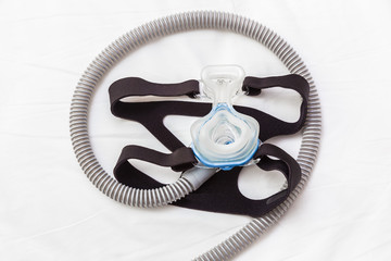 CPAP mask, connecting with strap and hose laying on a bed, helping snoring people with respiratory...