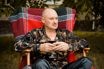 Fototapeta premium Mature stylish man tasting a glass of red wine, traditional red plaid at autumn . Alone seniors smelling a glass of red wine. Thinking about life and problems with wine