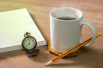 Black coffee with a notebook on a brown table. In the morning and Vintage clock at 8 o’clock.