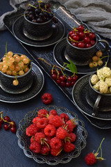 Composition of fresh ripe berries: red, black and white currant, mulberry on a dark gray concrete background. Dark photo. Photographing in natural light. Space for your text