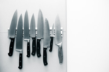 Kitchen knives set on a magnet on a light wall for background. Toned