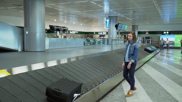 Young adult woman wait and pick up suitcase from luggage belt